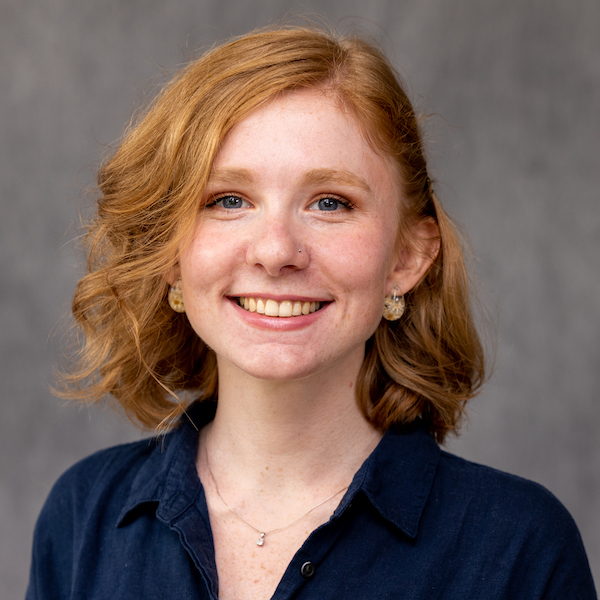 A headshot of SIS student Grace Moore. She has chin length curly red hair and is smiling at the camera.