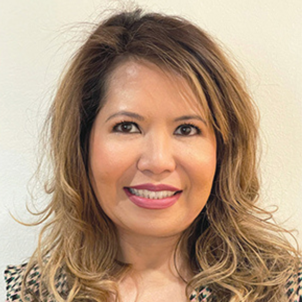 A headshot of SIS alumna Regina Gong. She has long, wavy light brown hair and is wearing a black and white patterned blouse.