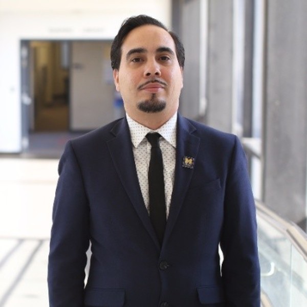 Edras Rodriguez-Torres is pictured standing in a dark blue suit with a matching tie. He has dark brown hair and goatee. 