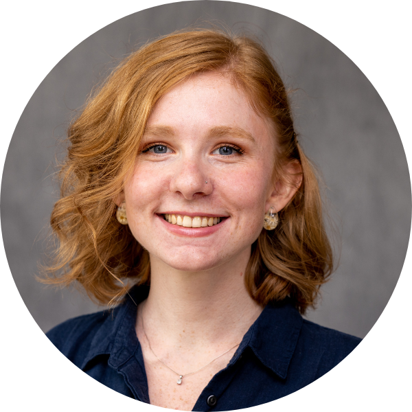 A headshot of SIS student Grace Moore. She has wavy red hair and is smiling at the camera.