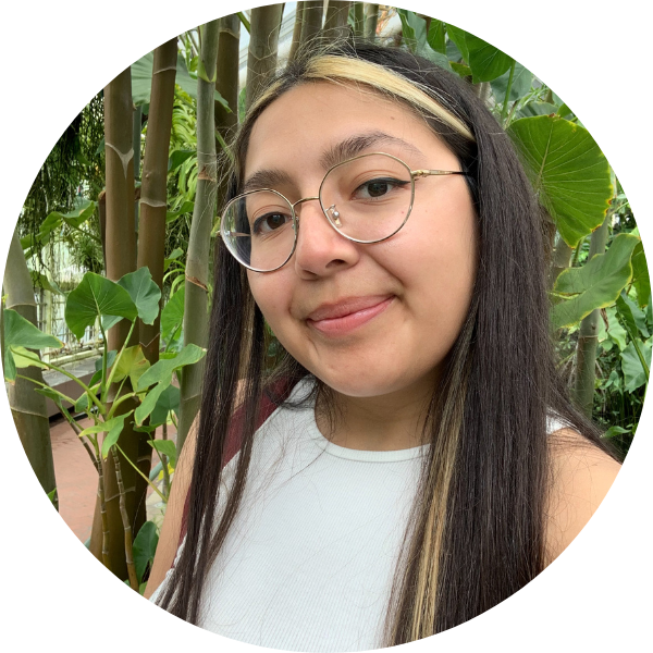 SIS student Selena Aguilera has long straight brown hair with a blonde streak in the front. She is taking a selfie with green plants in the background.